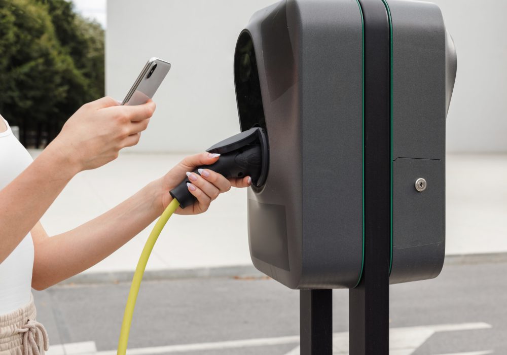 Girl connecting an electric car and charging station with a cable charger Girl connecting her electric car and a charging station with a cable charger and pressing a start button to activate a charging session