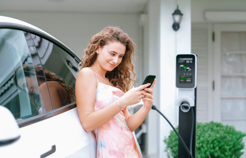 Modern eco-friendly woman recharging electric vehicle from home EV charging station. EV technology utilization for tracking energy usage to optimize battery charging at home. Panorama Synchronos